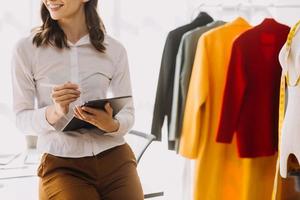 Beautiful lady blogger showing clothes in front of the camera to recording vlog video live streaming at her shop. Online Shopping Cart notion. photo