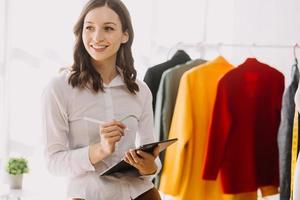 Beautiful lady blogger showing clothes in front of the camera to recording vlog video live streaming at her shop. Online Shopping Cart notion. photo