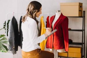Beautiful lady blogger showing clothes in front of the camera to recording vlog video live streaming at her shop. Online Shopping Cart notion. photo