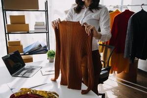 Beautiful lady blogger showing clothes in front of the camera to recording vlog video live streaming at her shop. Online Shopping Cart notion. photo