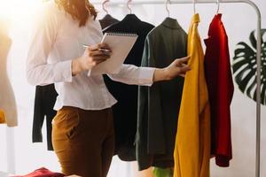Beautiful lady blogger showing clothes in front of the camera to recording vlog video live streaming at her shop. Online Shopping Cart notion. photo