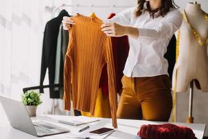 Beautiful lady blogger showing clothes in front of the camera to recording vlog video live streaming at her shop. Online Shopping Cart notion. photo