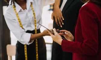 Diverse female fashion designers at work with tailor centimeters on necks and holds tablet and smartphone. independent creative design business. in studio photo