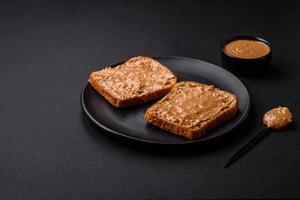 Nutritious sandwich consisting of bread and peanut butter on a black ceramic plate photo