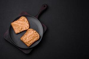 nutritivo emparedado consistente de un pan y maní mantequilla en un negro cerámico plato foto