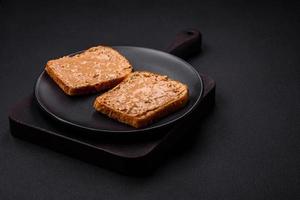 nutritivo emparedado consistente de un pan y maní mantequilla en un negro cerámico plato foto