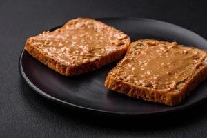 nutritivo emparedado consistente de un pan y maní mantequilla en un negro cerámico plato foto