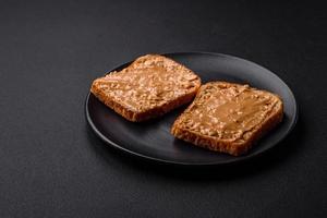 nutritivo emparedado consistente de un pan y maní mantequilla en un negro cerámico plato foto