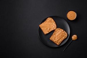 nutritivo emparedado consistente de un pan y maní mantequilla en un negro cerámico plato foto