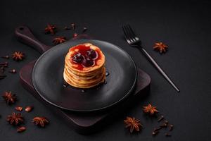 Delicious fresh pancakes with berry jam on a black ceramic plate photo