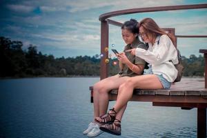 Social media and digital online concept, Two joyful cheerful girls using smart phone with Social media. The concept of living on vacation. Two young asia womens backpack to travel the holidays. photo