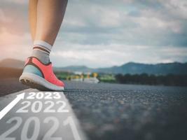 paso dentro 2023, hembra atleta caminando en blanco línea en la carretera con texto yendo mediante cada año y preparando a entrar el nuevo año foto