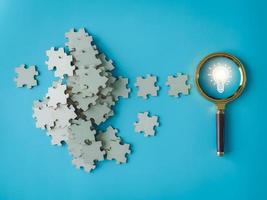 light bulb on a magnifying glass There is a pile of jigsaw puzzles. generating new ideas new business ideas photo