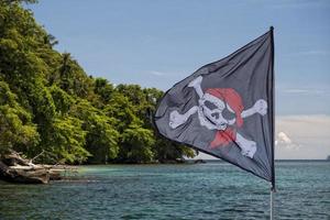 ondeando la bandera pirata jolly roger en el fondo de la isla tropical foto