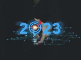 Businessman holding a lightbulb with a red goal in the middle on 2023. Start a new idea, a new project, a plan to deal with. Problems to achieve goals in the new year photo