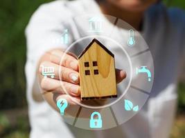 Young woman's hand holding a wooden house. Showing a model. Digital. Genius. Smart house technology, innovation of the future. photo