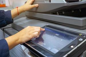 The secretary presses a finger on the keypad on the copier's screen to set up a print job to make multiple copies of a document. soft and selective focus. photo