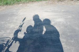 sombra de 3 personas en asfalto montando eléctrico bicicleta foto