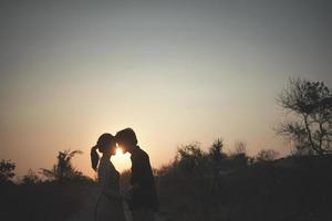 el silueta Pareja para pre boda, con un hermosa puesta de sol ver y silueta de colina antecedentes con árbol y césped foto