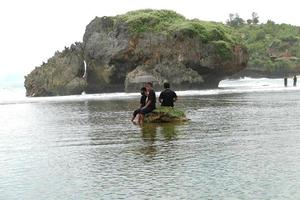 padre con paraguas y 2 hijos sentado en un rock por el playa con grande rock antecedentes , kuk up playa a noviembre 27, 2022 Gunung kidul, yogyakarta, Indonesia foto