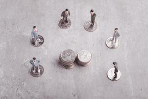 Miniature people standing around coins, business man shaking hands during a meeting, success, dealing, greeting and partner concept. photo