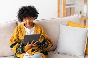 African american girl holding digital tablet touch screen typing scroll page at home. Woman with mobile tech device surfing internet using social media apps playing game. Study work shopping online. photo