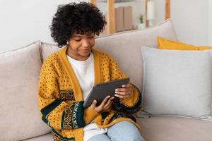African american girl holding digital tablet touch screen typing scroll page at home. Woman with mobile tech device surfing internet using social media apps playing game. Study work shopping online. photo