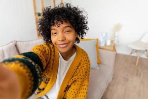 Happy african american teen girl blogger smiling face talking to webcam recording vlog. Social media influencer woman streaming making video call at home. Headshot portrait selfie webcamera view. photo