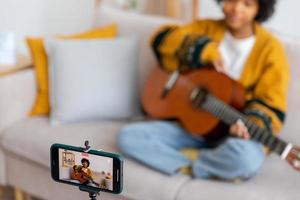 Blogger guitarist. Happy african american girl blogger playing guitar singing song recording vlog. Social media influencer woman streaming recording at home studio. Music content creator broadcast. photo