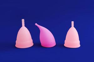 three different pink reusable silicone menstrual cup isolated on blue background. Concept of feminine hygiene, photo