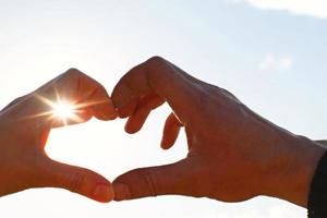 Two hands, male and female, are joined in the shape of a heart against the sky with the sun's rays at the opening. Symbol of a couple in love, Valentine's day, romance, wedding in heaven. copyspace photo