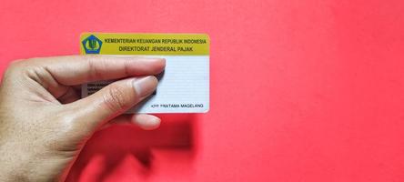 Man holding npwp or indonesian tax card isolated on a red background, negative space. photo