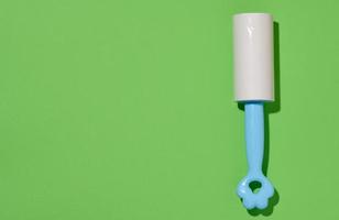 Roller with sticky tape for cleaning clothes on a green background, top view photo