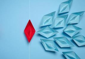 A group of blue paper boats and one red sailing against the current, concept of independent personality, breaking free from influence, strong leadership photo