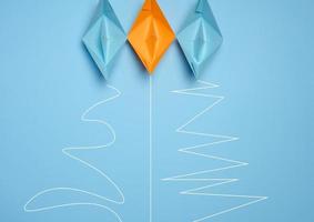 Three paper boats with different trajectories on a blue background, concept of goal achievement differences, effectiveness photo