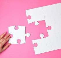 female hand puts white big puzzles on a pink background photo