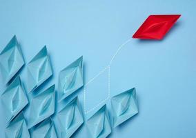 A group of blue paper boats and one red one moving in the opposite direction, the concept of independent personality and breaking away from influence photo