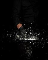 Chef in black uniform holds a pan with white salt and throws up photo