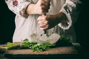 woman in a gray linen dress is cutting green leaves of fresh sorrel on a wooden cutting board photo