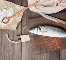 fresh whole sea bass fish and knife on brown cutting board photo