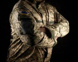 Ukrainian soldier in camouflage uniform stands with arms crossed on his chest photo