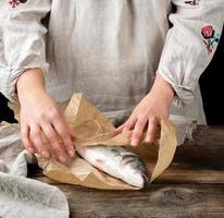 female hands are wrapped in paper whole sea bass fish photo