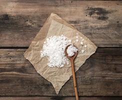 large white salt on a brown piece of paper and a wooden spoon photo