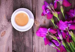 taza de café y un ramo de flores de púrpura iris en un gris de madera superficie foto