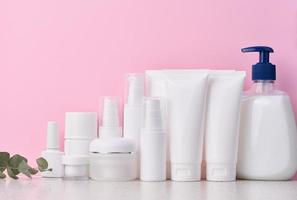 White plastic tubes, jars, and containers for cosmetic products on a pink background, advertising and branding of products photo