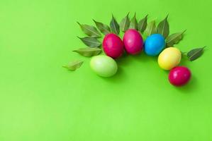 Pattern of colored eggs and green leaves on a green background. Copy space for text. Bright colours. Easter. photo