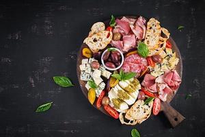 Antipasto platter with ham, prosciutto, salami, blue cheese, mozzarella with pesto and olives on a wooden background. Top view, overhead photo