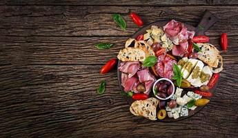 Antipasto platter with ham, prosciutto, salami, blue cheese, mozzarella with pesto and olives on a wooden background. Top view, overhead photo