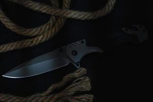 Tactical folding knife for survival, active lifestyle and recreation, on rope background and dark background. photo