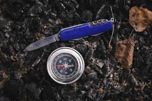 Penknife and a compass on the coals an extinguished campfire, picnic, recreation and adventures in wild. photo